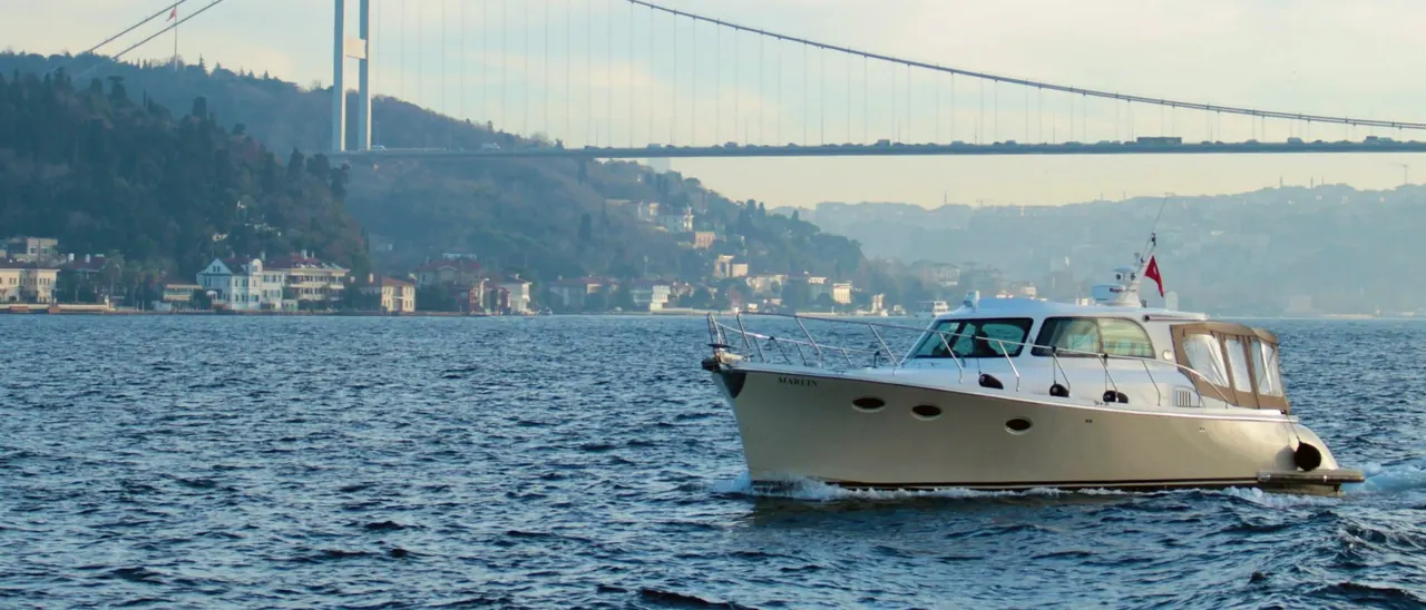 A private motor yacht under way on the Bosphorus, below the bridge and the wooded shore