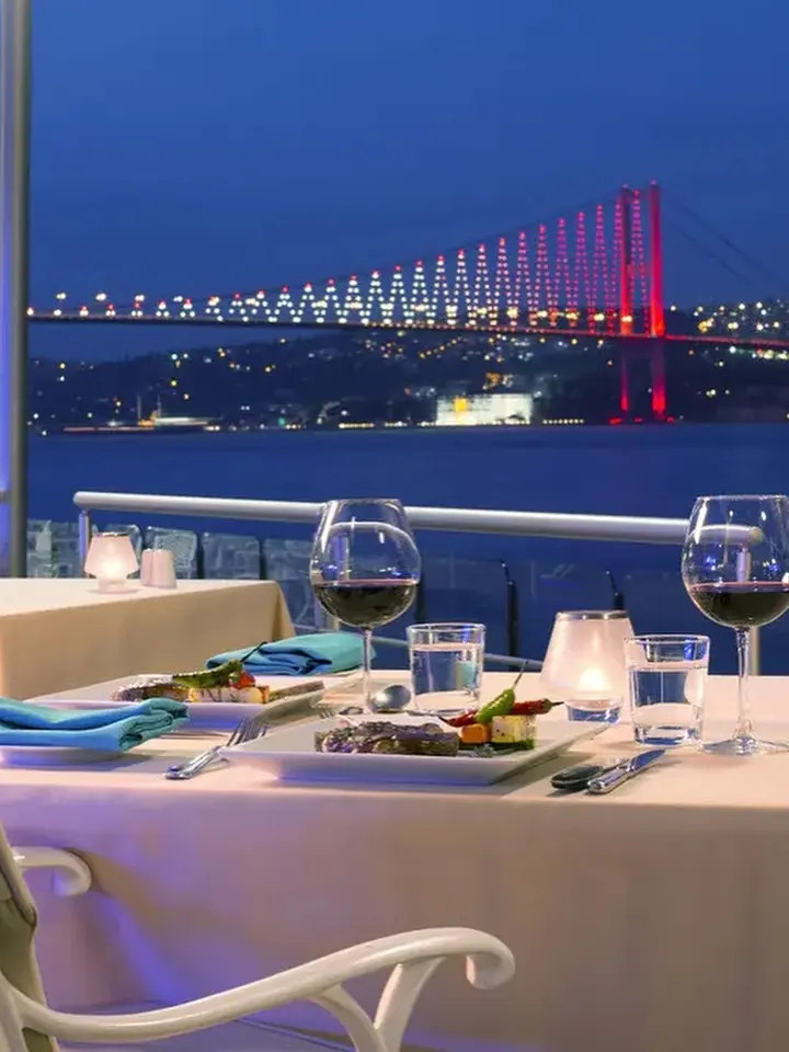 A table laid for two on a terrace above the Bosphorus at night, the bridge lit behind