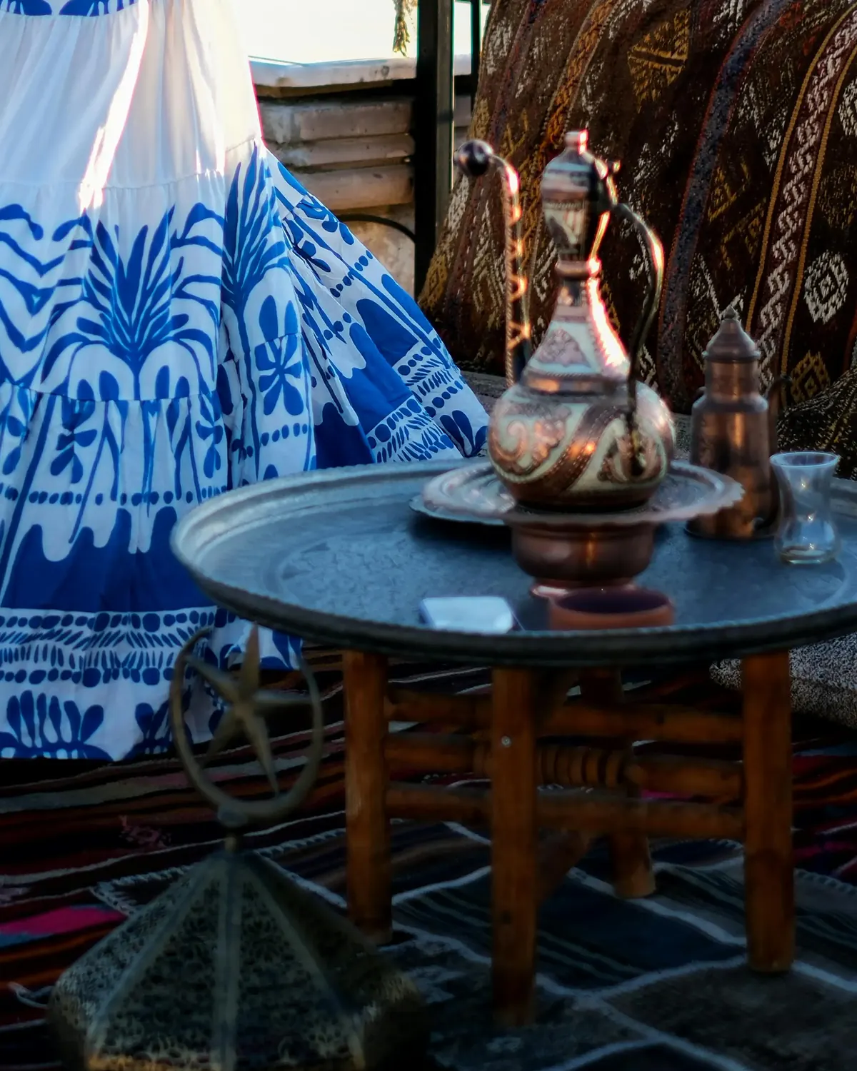 A copper ewer on a tray table on a terrace in Cappadocia, kilims underfoot, in early light